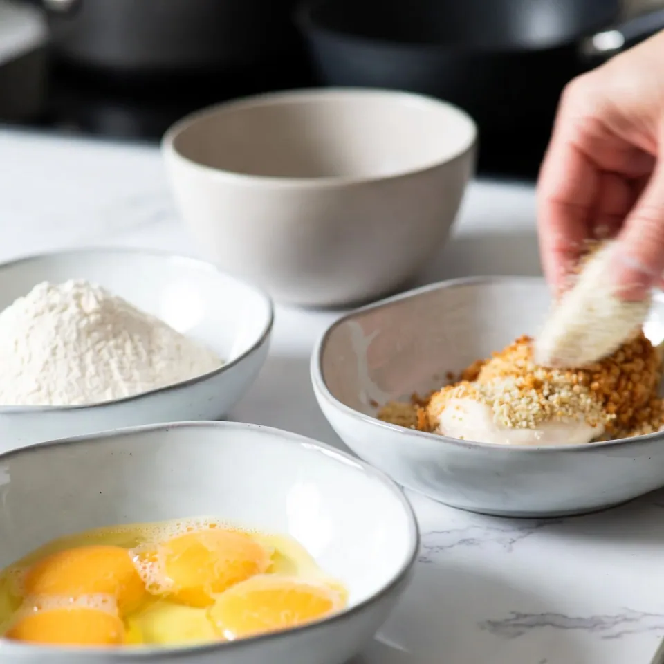 Chicken is being coated in breadcrumbs